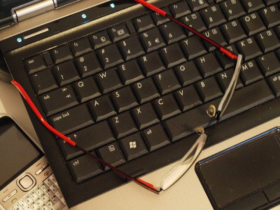 A black computer keyboard with red-framed glasses on top.