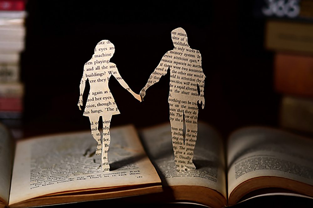 Image: two silhouetted figures cut from pages of separate books, pushed close together and holding hands