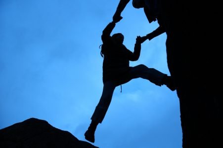 Image: silhouette of one hiker helping another up the cliff face
