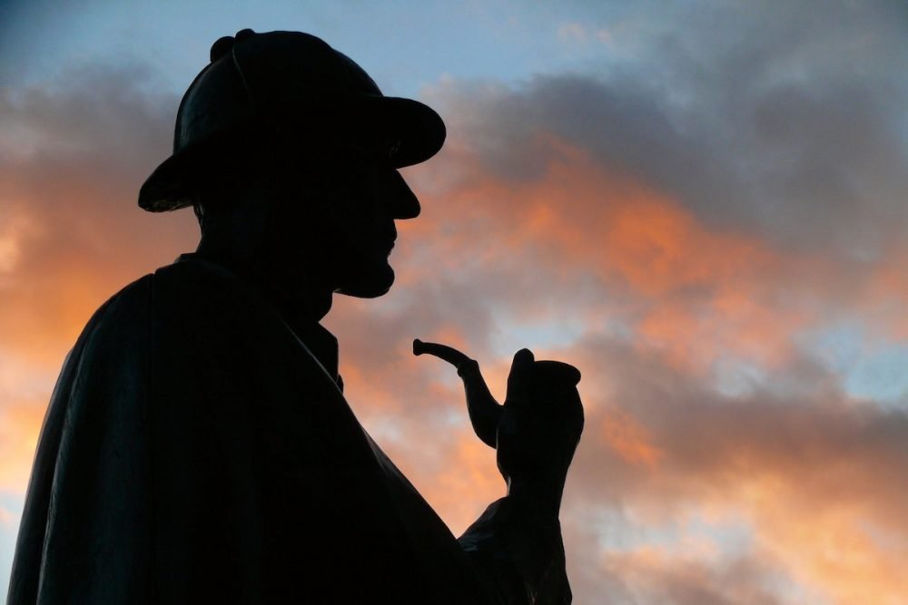 Image: Sherlock Holmes statue silhouetted against a colorful evening sky.