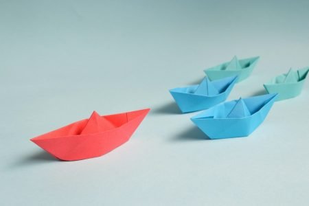 Image: five origami boats. Four smaller boats follow a larger one.
