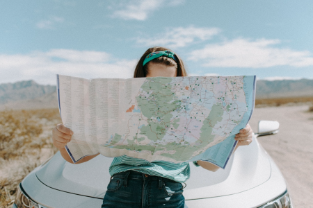 Alone on a deserted road, a woman leans against the front of her car while examining a road map.
