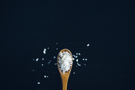 Image: a small wooden spoon holding grains of salt.