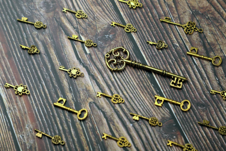 Image: ornately decorated, gold-colored antique keys are arranged on a wooden table.