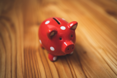 Image: a small piggy bank, painted bright red with white polka dots, sits on a wooden table.