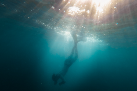 Image: an underwater photo of a diver heading into the depths.