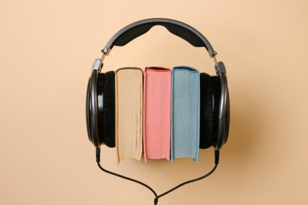 Image: three hardcover books, stacked together and viewed from their top edges, are sandwiched between a pair of over-the-ear headphones.
