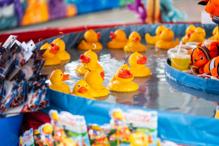 Image: dozens of identical plastic yellow ducks with hooks attached to their heads float in circular pool of water in a fairground game.