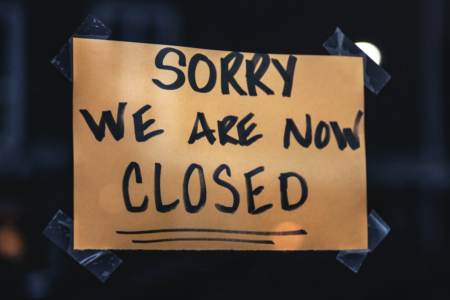 Image: a hastily-made sign written in marker on brown paper and taped to a window reads "Sorry we are now closed."