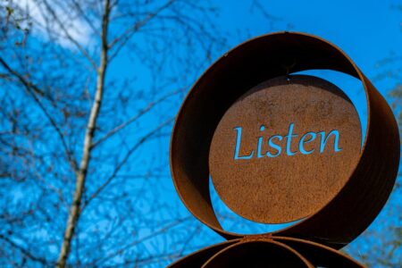 Image: at the Sculpture by the Lakes park in Dorchester UK, a rusted metal artwork has the word "Listen" cut out so that the deep blue sky shows through.