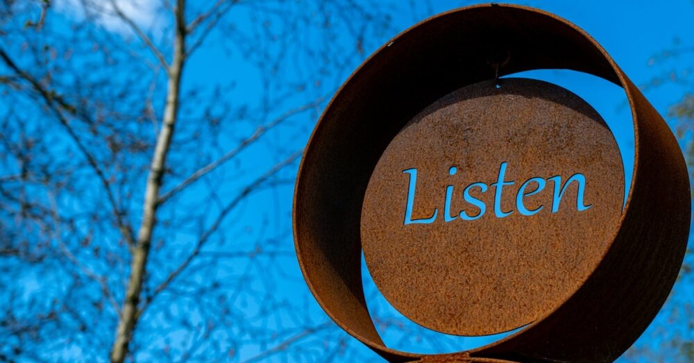 Image: at the Sculpture by the Lakes park in Dorchester UK, a rusted metal artwork has the word "Listen" cut out so that the deep blue sky shows through.