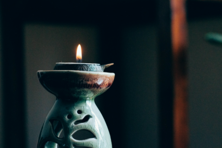 Image: a lit tea candle in a holder against a dark background