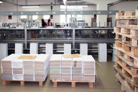 Image: book binding materials are stacked on pallets beside the finishing line of a book factory.