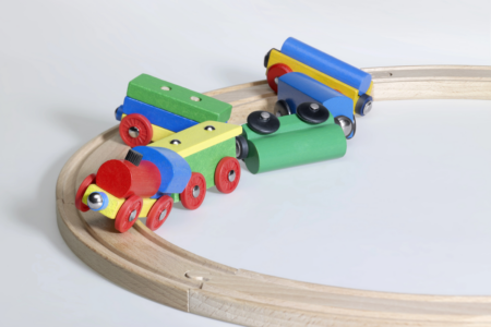 Image: the colorful railcars of a child's toy train are derailed from its wooden track.