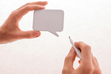 Image: a man's hand holds a cut-out in the shape of a speech bubble, while his other hand holds a pen preparing to write a message on it.