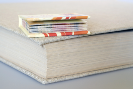 Image: a miniature hardcover book sits atop a standard sized one