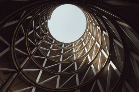 Image: looking up at a circle of blue sky from within the center of a circular parking garage.