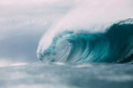 Image: white foam tops the teal waters of a dramatically-arced ocean wave.
