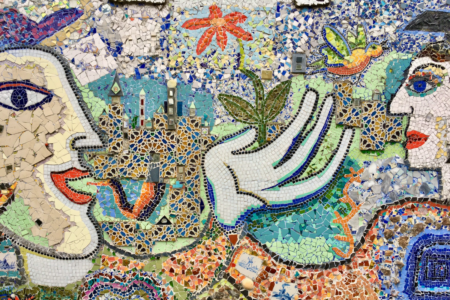 Image: a colorful mosaic in Amsterdam depicting two figures surrounded by flora, fauna, and architecture, made from many different types of tile.