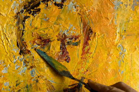 Image: a painter uses a palette knife to add color to a heavily-textured canvas so that facial features begin to emerge from abstraction.