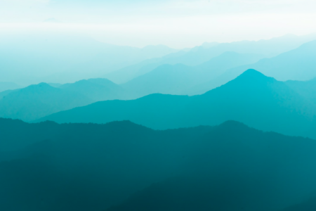 Image: layers of a mountain range, appearing as darker-to-lighter shades of blue, disappear into the misty distance.