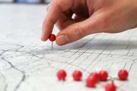Image: a hand is applying a single red pin to a point on a map