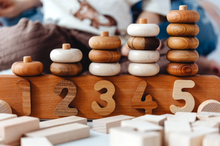 Image: a child's counting toy made of doughnut-shaped wooden rings stacked on dowels, in quantities of 1, 2, 3, 4 and 5.