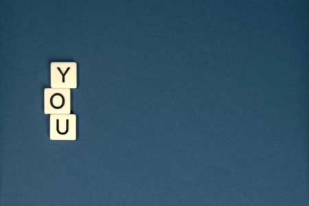Image: Scrabble-style tiles of the letters Y-O-U on a blue background.