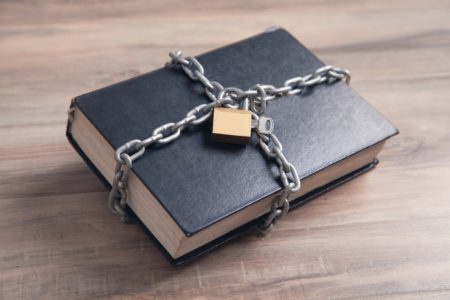 Image: a black hardcover book is bound in chains and secured with a padlock.