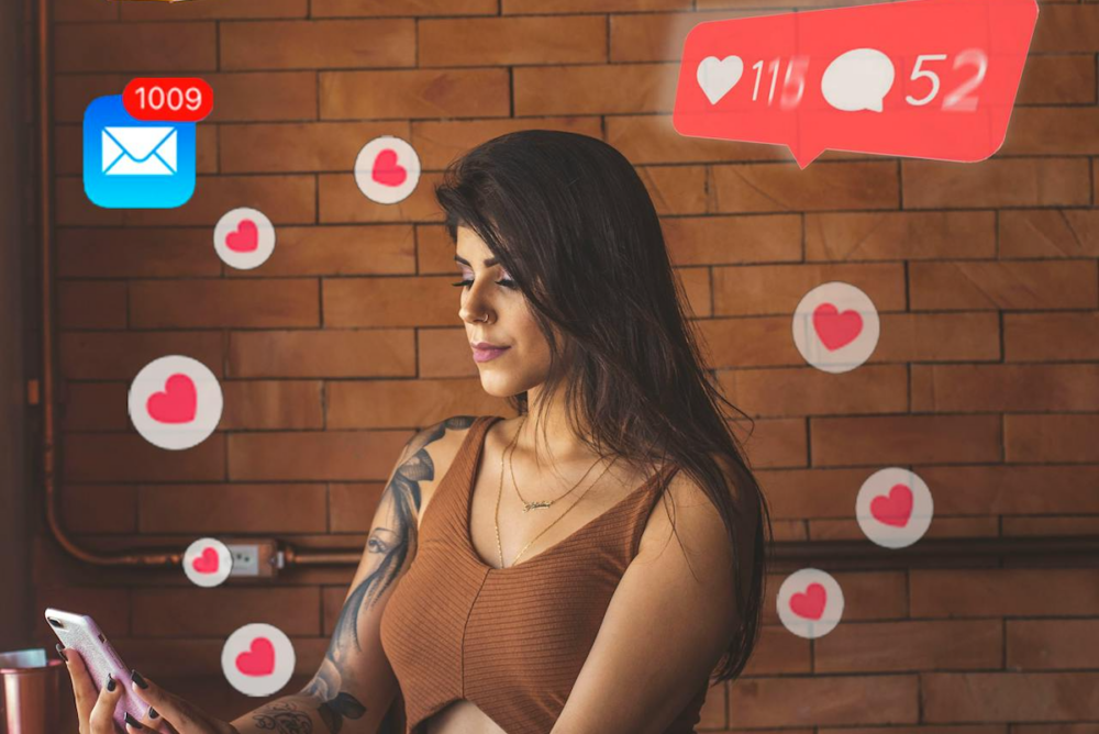 Image: a woman sits looking at her smartphone. In the air around her are icons representing social media reactions, and email and phone notifications.