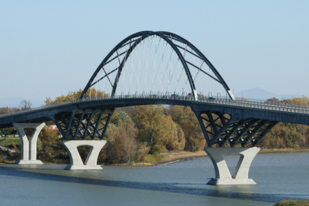 Image: a bridge with a suspension arch in the middle spans a river.