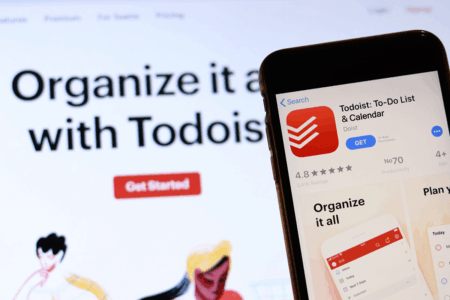 Image: a smartphone displaying the Todoist app's page in the app store hovers in front of a laptop's browser window displaying the Todoist homepage.