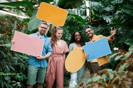 Image: four young adults of varying ethnicities hold differently shaped and colored placards in the style of cartoon word balloons.