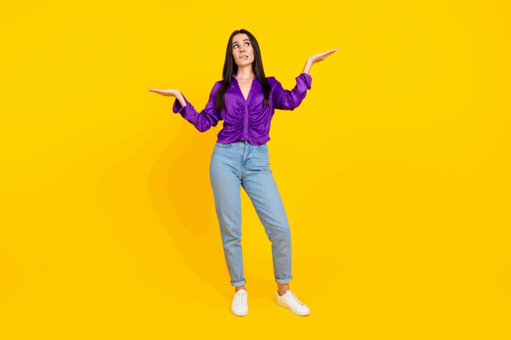 Image: against an empty backdrop, a woman wearing a quizzical expression stands with her hands in the air in the manner of a scale weighing two unseen options.