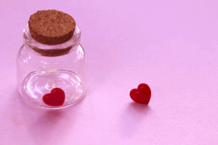 Image: one miniature heart is trapped in a jar while another sits outside it, longing for reunion.