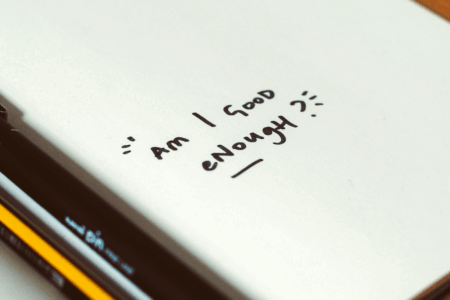 Image: in an open notebook flanked by pens and pencils are the handwritten words, "Am I good enough?"