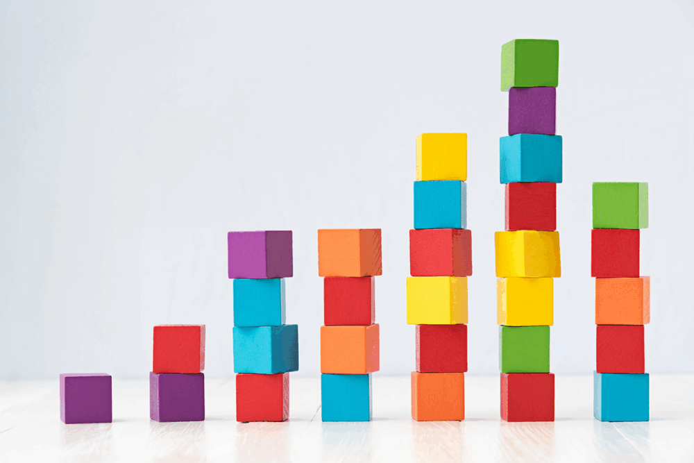Image: colorful wooden blocks are stacked in increasingly higher vertical columns which mimic a book's rising story structure.