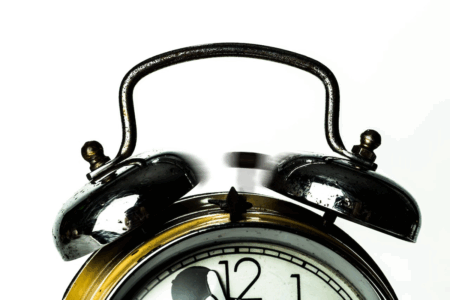 Image: an analog alarm clock chimes, indicated by the hammer moving rapidly between the bells.