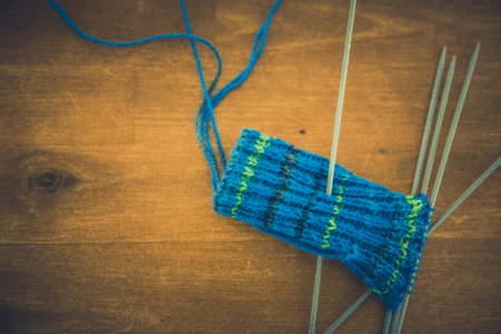 Image: a knitting project in progress made of blue, yellow and black yarn.