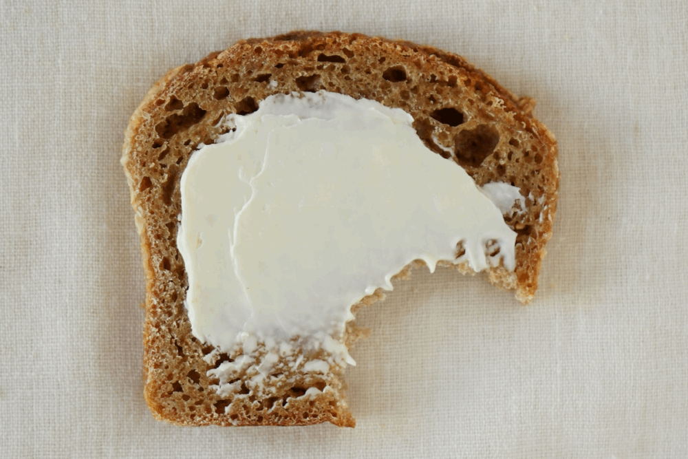 Image: a slice of brown bread that's smeared with butter has had a bite taken out of it.