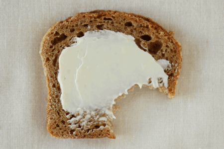 Image: a slice of brown bread that's smeared with butter has had a bite taken out of it.