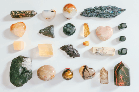 Image: an assortment of differently-hued natural stones, crystals, and minerals are arranged in neat rows on a white surface, representing a themed collection composed of related but varied pieces.
