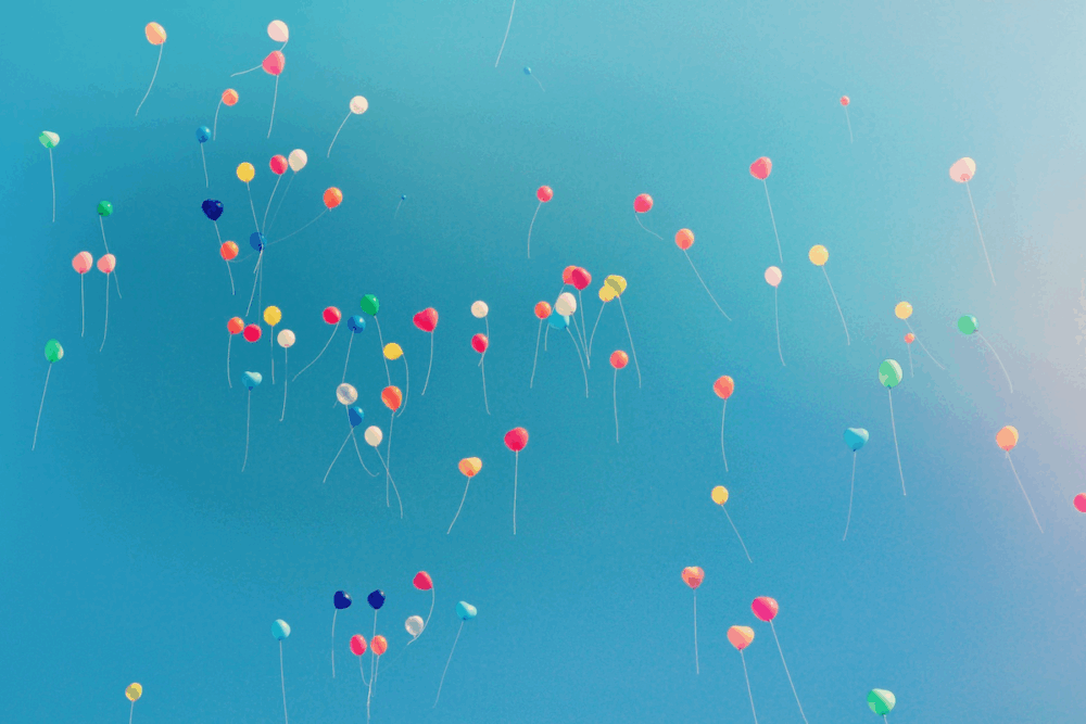 Image: scores of colorful balloons float up into a clear blue sky.