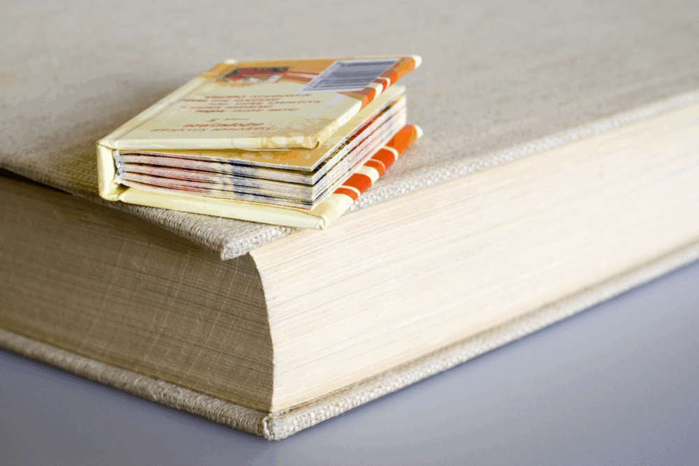 Image: a miniature hardcover book, only about an inch wide, rests atop a standard sized hardcover book.