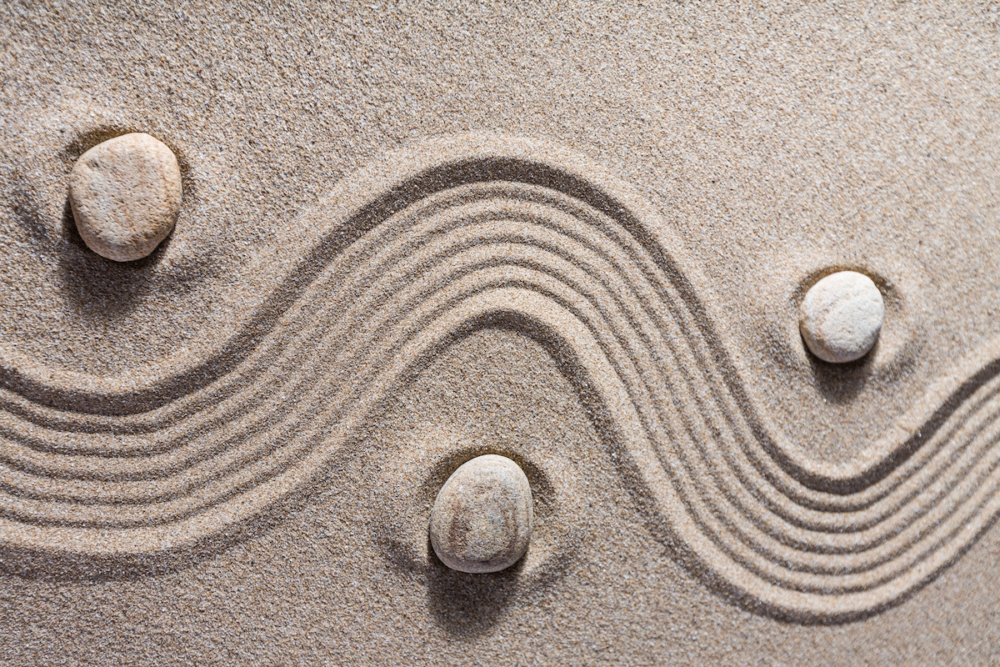 Image: overhead view of a zen sand garden in which a raked S-curved path snakes among three stones.