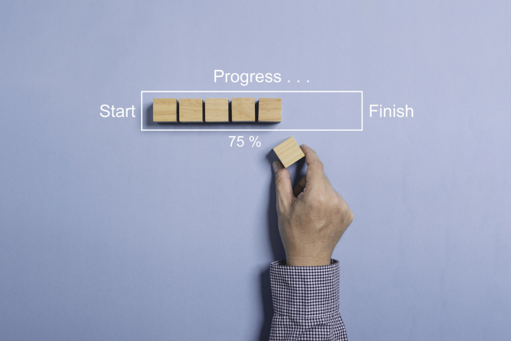 Image: a row of wooden blocks represent a website progress bar. A white box is drawn around the blocks with the word Start at the left end, Finish at the right end, and 75% as the completion level. A man's hand adds a wooden block to the row.