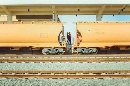 Image: seen between cars of a train stopped at a station, a man and woman are seen standing on the railway platform.