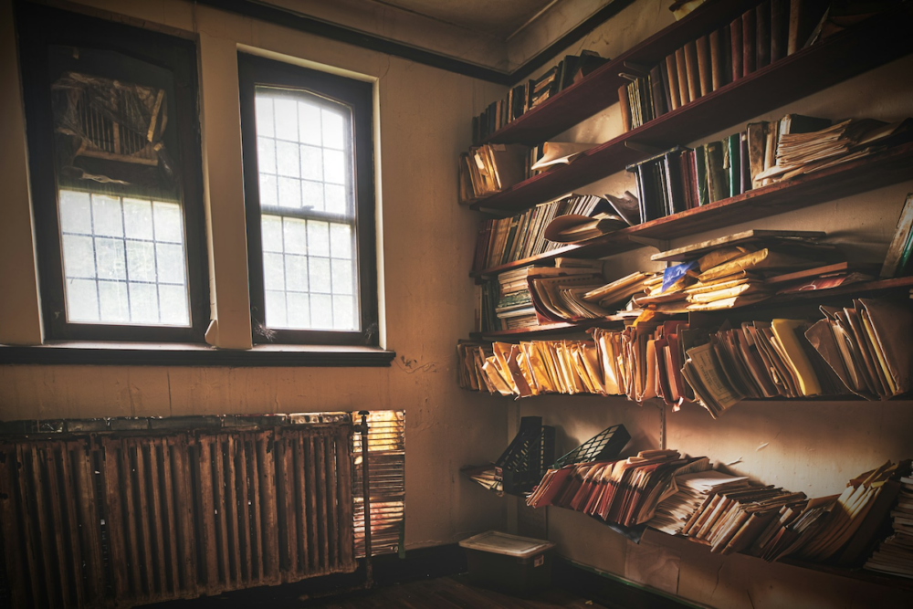 Image: light streams through windows onto messy shelves full of disorganized files, envelopes, and books.