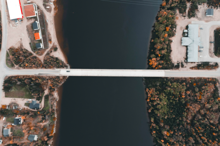 Image: seen from an aerial view, a single car drives across a bridge that connects two sides of town across a waterway.