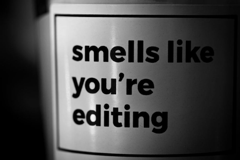 Image: black and white photo of a scented candle whose label reads, "Smells like you're editing."